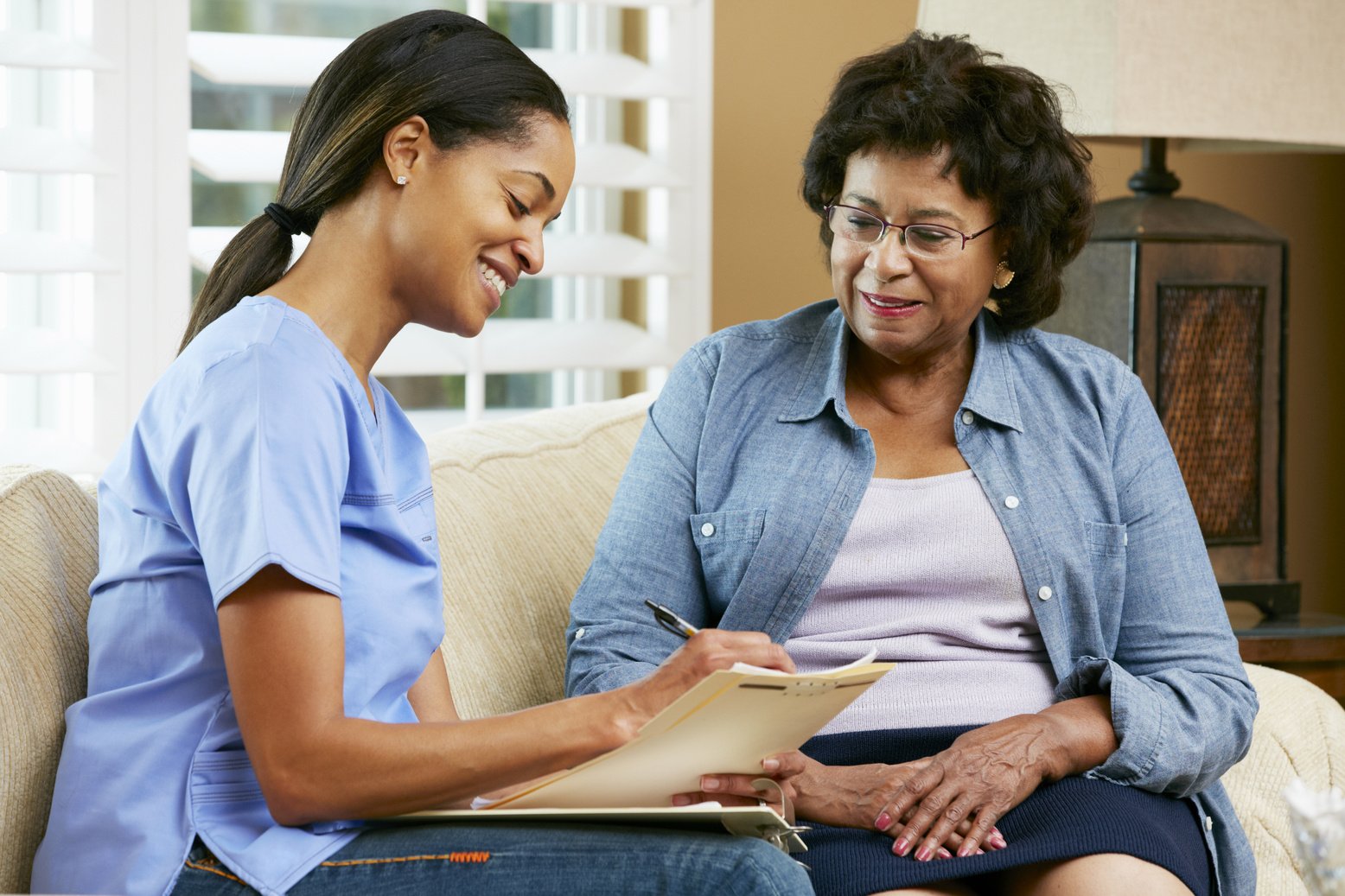 Nurse Making Notes during Home Visit with Senior Female Patient